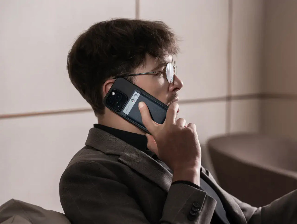 Un homme en costume gris parle au téléphone, avec un Plaud Note gris fixé à l'arrière de son smartphone.