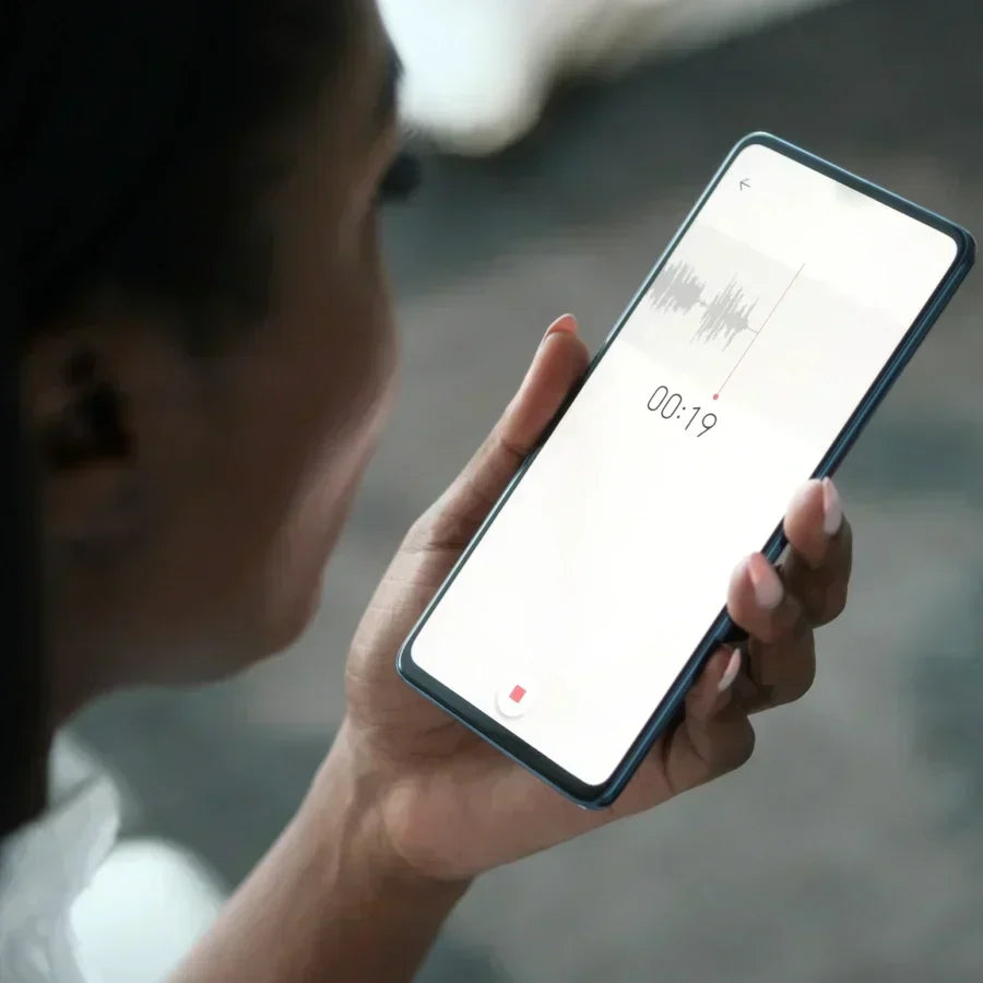 Une personne tient un smartphone affichant l'interface d'enregistrement de l'App Plaud avec une forme d'onde et un minuteur.