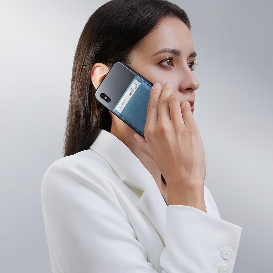 Une femme en blazer blanc parle au téléphone, un Plaud Note argenté fixé à un porte-cartes bleu sur son smartphone.