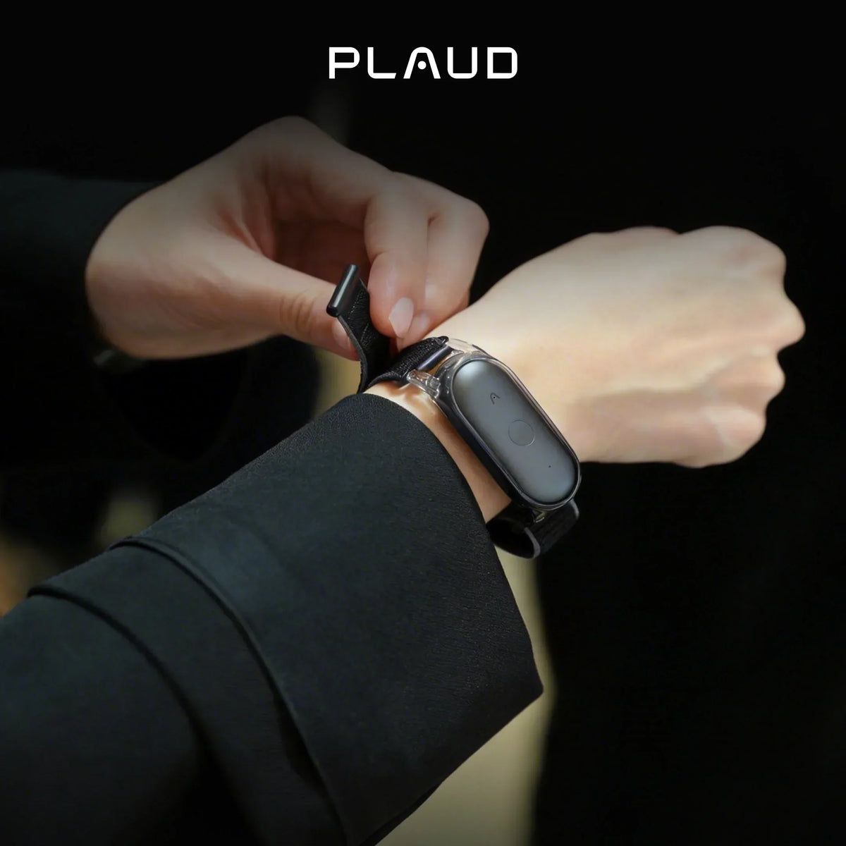 Une personne attache un bracelet noir avec un Plaud NotePin S noir à son poignet, sur un fond sombre.