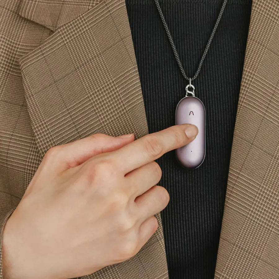 Une personne touche un Plaud NotePin violet porté en collier sur un blazer marron à carreaux