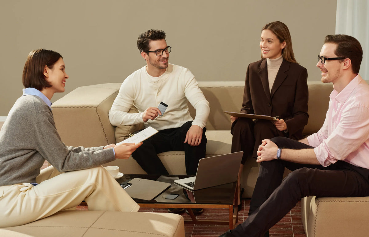 Quatre personnes souriantes discutent dans un salon, l'une tenant un Plaud Note Pro noir.