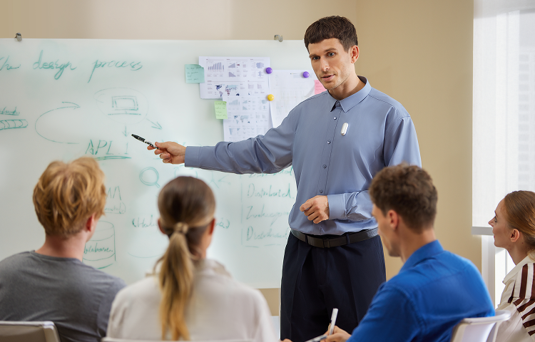 Un homme en chemise bleue présente devant un tableau blanc, avec un Plaud NotePin blanc épinglé à sa chemise