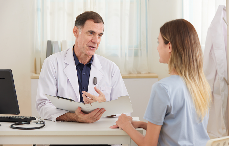 Un médecin en blouse blanche parle à une patiente dans son bureau, avec un Plaud NotePin gris accroché à sa blouse.