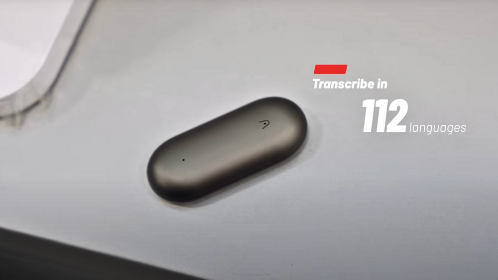 Un Plaud NotePin gris foncé est posé sur une surface grise, illustrant sa capacité à transcrire en 112 langues.