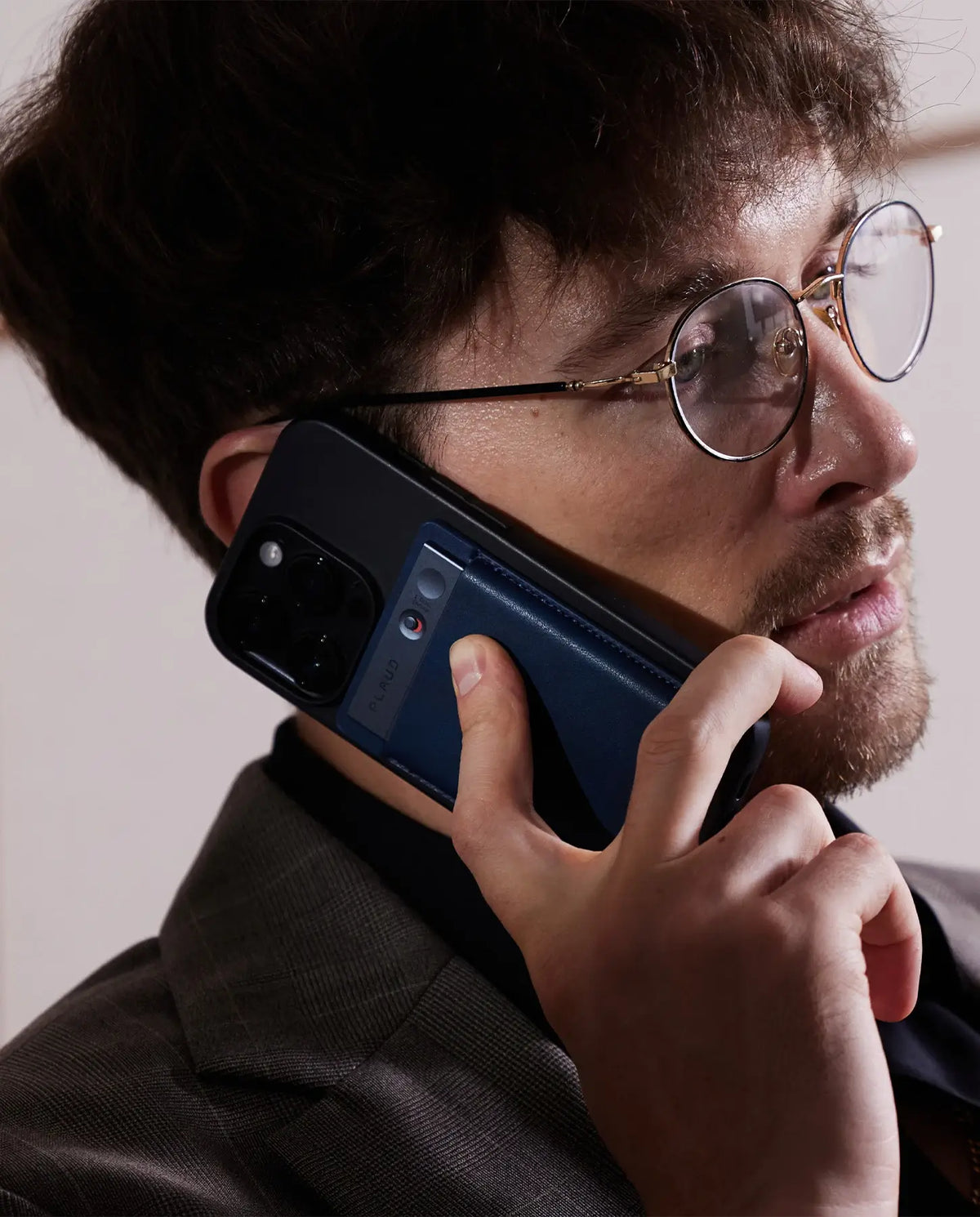 Un homme en costume parle au téléphone, avec un Plaud Note bleu foncé attaché discrètement à l'arrière de son smartphone.