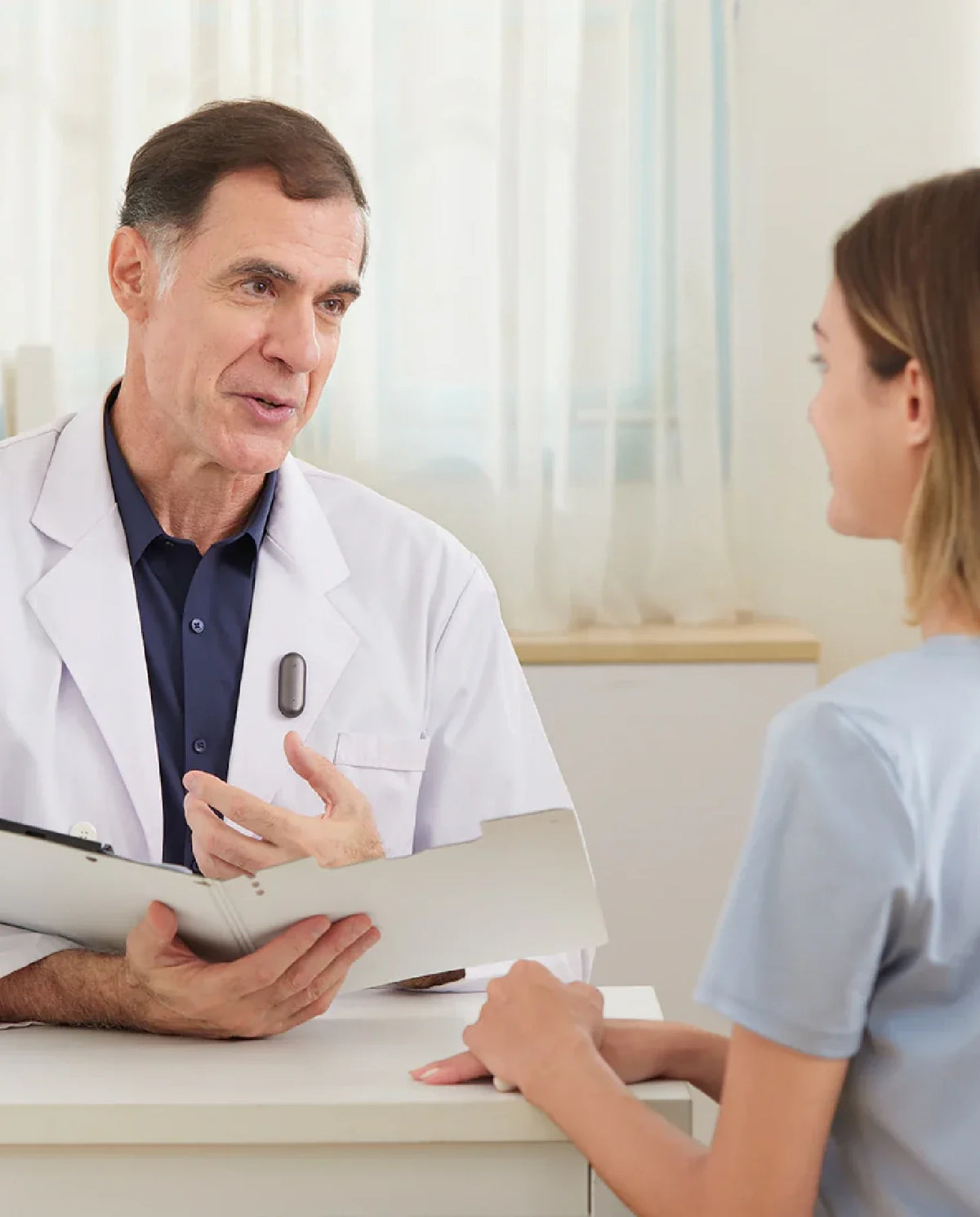 Un médecin portant un Plaud NotePin S gris foncé sur sa blouse blanche explique des informations à une patiente attentive.