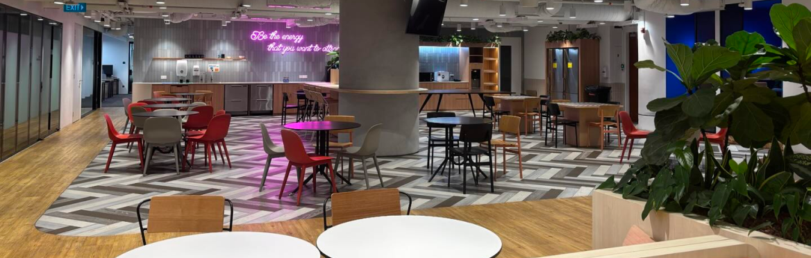 Grand espace de bureau moderne avec des tables et chaises colorées, un sol en bois et à motifs, et un néon rose.