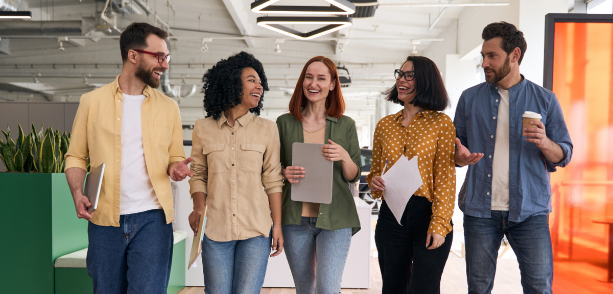Cinq collègues souriants et diversifiés marchent et discutent dans un bureau moderne et lumineux.
